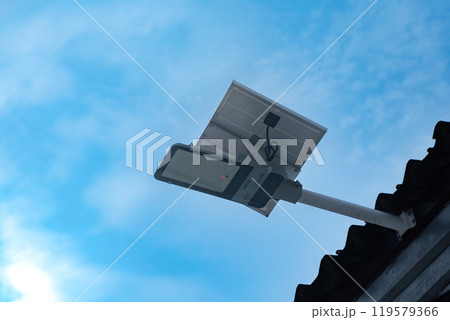 Mini solar cell panel and hd floodlight panal installed together under house eaves to store and use the power from the sunlight with street light and bulbs at night, sunset background, soft focus. Mini solar cell panel and hd floodlight panal installed together under house eaves to store and use the power from the sunlight with street light and bulbs at night, sunset background, soft focus. 119579366