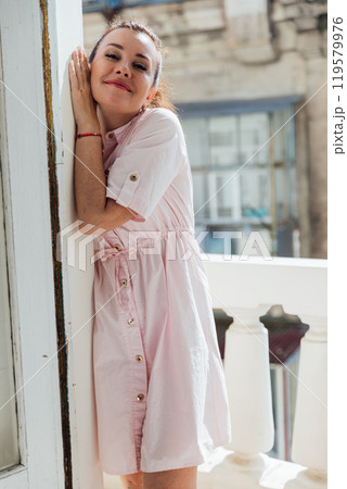 Beautiful woman in summer light dress standing on balcony and smiling 119579976