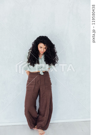Curly brunette woman standing near a white wall Curly brunette woman standing near a white wall 119580438