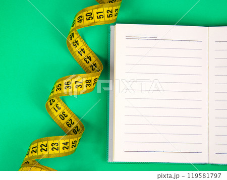 Yellow tape measure centimetric with paper note on green background Yellow tape measure centimetric with paper note on green background 119581797