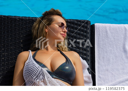 Pretty young woman lying on sun lounger near swimming pool Pretty young woman lying on sun lounger near swimming pool 119582375