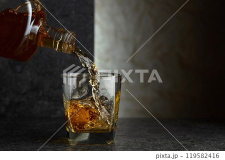 Pouring whiskey from a bottle into a glass. 119582416