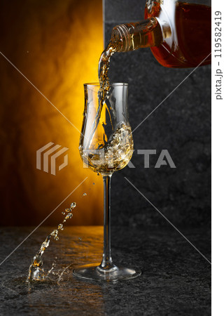 Pouring strong alcoholic drink from a bottle into a glass. 119582419