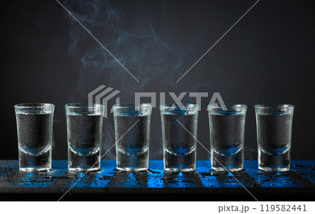 Alcoholic shots of tequila or strong drink in small wet glasses on a black table. Alcoholic shots of tequila or strong drink in small wet glasses on a black table. 119582441