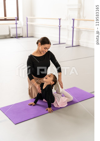 Cute little ballerina practicing ballet with her teacher in studio doing stretching Cute little ballerina practicing ballet with her teacher in studio doing stretching 119583165