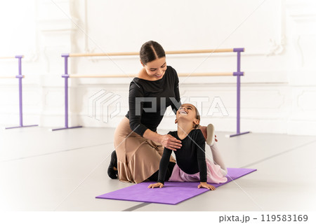 Cute little ballerina practicing ballet with her teacher in studio doing stretching 119583169