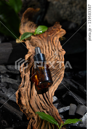 The simple background of the photo-chic advertisement is created by an amber glass dropper bottle placed in the center on a piece of worn wood, encircled by tiny bits of charcoal and leaves. 119583387