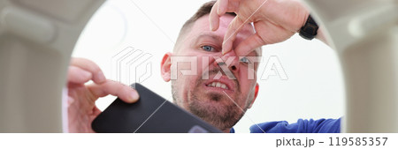 Man takes phone out of toilet bowl pinching nose in disgust 119585357