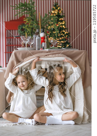 Little sisters hiding under the Christmas table. On the eve of the New Year and Christmas 119585722