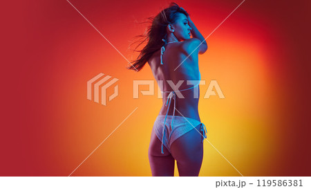 Rear view photo of woman in bikini stands, posing confidently in neon light against gradient studio background. Rear view photo of woman in bikini stands, posing confidently in neon light against gradient studio background. 119586381