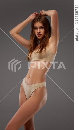 Young female model in posing,raising hands up, highlighting slim physique and natural beauty. against warm grey background. Young female model in posing,raising hands up, highlighting slim physique and natural beauty. against warm grey background. 119586734