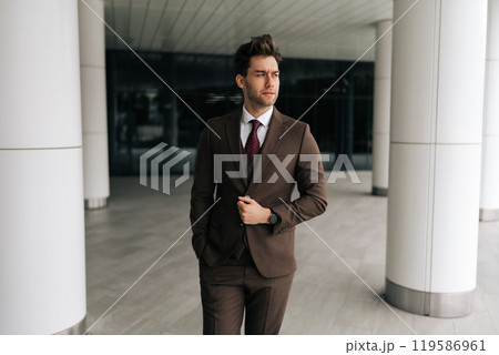Portrait of confident successful businessman adjusting jacket while walking in modern office building, conveying sense of purpose and determination, looking away with serious expression, 119586961