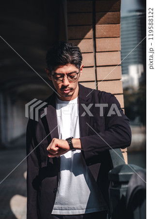 待ち合わせ中に時計を見るメガネをかけた男性 待ち合わせ中に時計を見るメガネをかけた男性 119588122