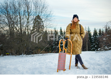 Portrait young adult happy woman enjoy having fun riding vintage wooden retro sledge mountain hill cold winter sunny day. Female joyful person sledding downhill outside at Christmas season Portrait young adult happy woman enjoy having fun riding vintage wooden retro sledge mountain hill cold winter sunny day. Female joyful person sledding downhill outside at Christmas season 119588146