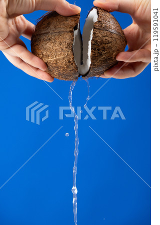 Hands open coconut, coconut water pour out, blue background 119591041