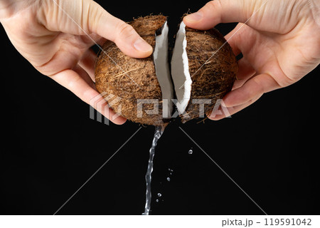 Hands open coconut, coconut water pour out, black background Hands open coconut, coconut water pour out, black background 119591042