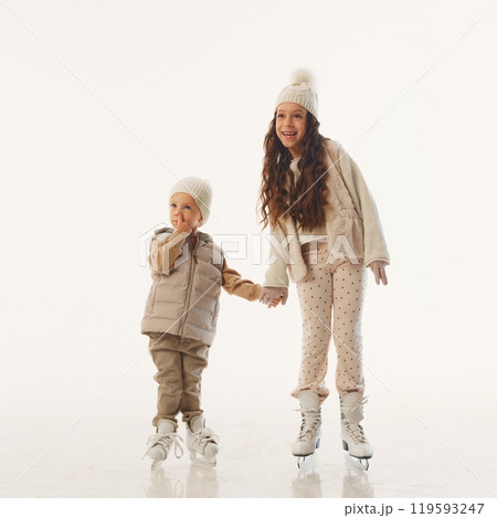 Laughing and playful, siblings share sweet hug during their Christmas ice skating session against white studio background. 119593247