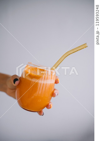 Refreshing orange smoothie served in a glass with a reusable straw on a plain background Refreshing orange smoothie served in a glass with a reusable straw on a plain background 119593248