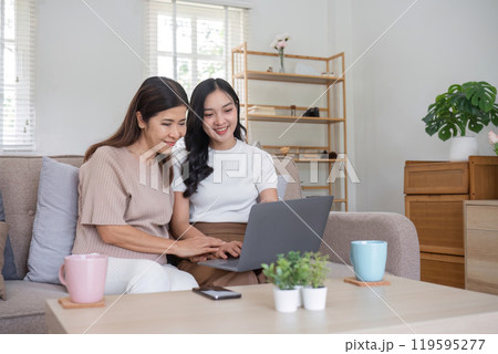 Elderly Mother and Daughter Enjoy Quality Time Together at Home, Smiling and Using a Laptop in a Cozy Living Room Setting 119595277