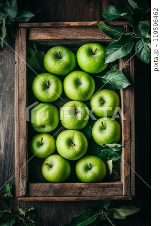 Fresh green apples arranged neatly in a rustic wooden crate with leaves on a dark background 119596462