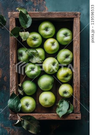 Fresh green apples arranged neatly in a rustic wooden crate with leaves on a dark background 119596533