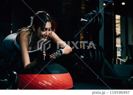 Asian woman guy performing doing bosu ball exercises and check time on smart watch in gym interior, sportswoman doing training balance body at fitness gym center, sport workout healthy lifestyle 119596997