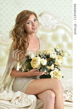 Beautiful young girl with a bouquet of flowers posing on the bed 119596998