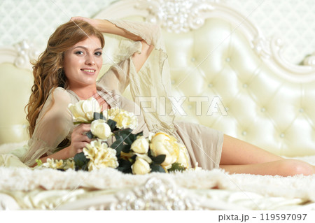 Beautiful young girl with a bouquet of flowers posing on the bed 119597097