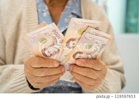 Asian elderly woman holding Thai banknotes money in hand. Poverty, saving problem in retirement. Asian elderly woman holding Thai banknotes money in hand. Poverty, saving problem in retirement. 119597653