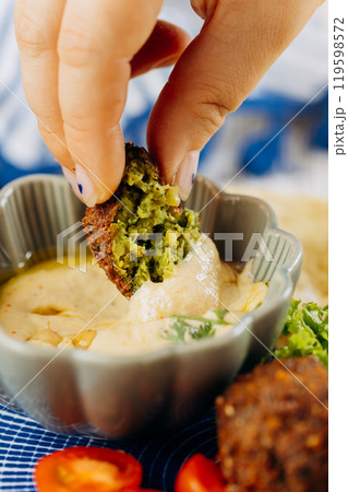 Dipping a crunchy falafel in creamy hummus for a delicious, plant based Mediterranean snack Dipping a crunchy falafel in creamy hummus for a delicious, plant based Mediterranean snack 119598572