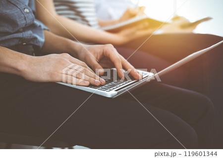 Group of casual dressed business people working at meeting or conference in sunny office, close-up of hands. Businessman using tablet computer 119601344