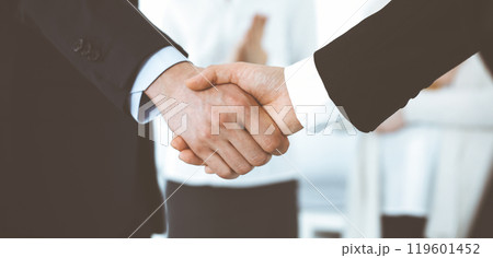 Businessman and woman shaking hands with colleagues at the background. Handshake at meeting in office. Concept of success in business 119601452