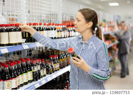 Woman customer is thinking about buying spicy and unusual soy sauce. Woman customer is thinking about buying spicy and unusual soy sauce. 119607753