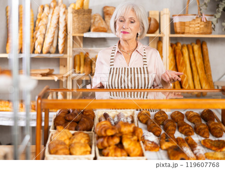 senior bakery worker sells croissants, demonstrates many different crescent-shaped buns senior bakery worker sells croissants, demonstrates many different crescent-shaped buns 119607768