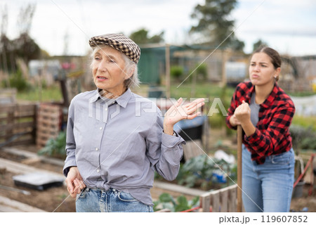 Two angry casual women neighbors of different ages arguing during the vegetable garden season on sunny day of spring Two angry casual women neighbors of different ages arguing during the vegetable garden season on sunny day of spring 119607852