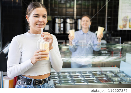 Girl bought bubble tea, drinks refreshing beverage near counter of cafeteria 119607875