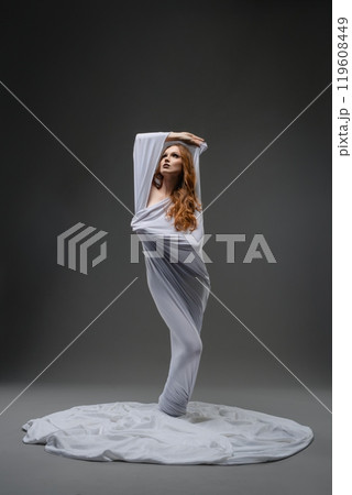 A dancer in a flowing white fabric striking an elegant pose in a studio A dancer in a flowing white fabric striking an elegant pose in a studio 119608449
