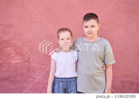 Siblings smiling together in front of a red wall outdoors on a sunny day Siblings smiling together in front of a red wall outdoors on a sunny day 119610389