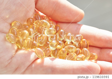 Close-up of hand holding yellow omega-3 fish oil capsules in sunlight for health 119610391