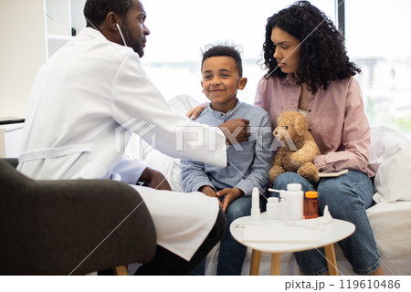 Doctor examining sick African boy with concerned mother at clinic 119610486