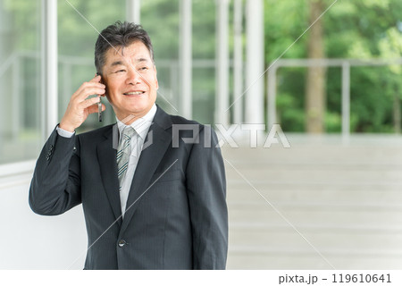 スマホで通話するスーツ姿のシニア世代の男性ビジネスマン スマホで通話するスーツ姿のシニア世代の男性ビジネスマン 119610641
