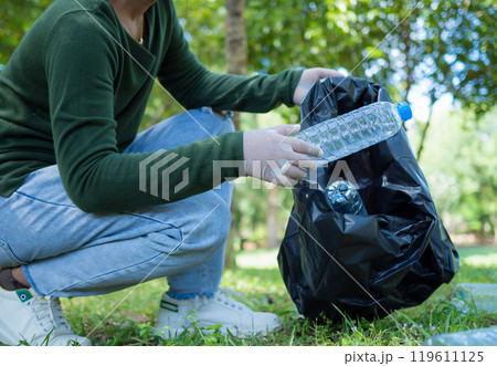 Woman of dedicated volunteers are participating in an environmental cleaning activity in a park. Woman wearing gloves and hold large black bags. Woman collecting trash and plastic bottles in a park. 119611125
