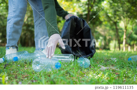 Woman of dedicated volunteers are participating in an environmental cleaning activity in a park. Woman wearing gloves and hold large black bags. Woman collecting trash and plastic bottles in a park. 119611135