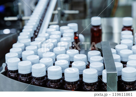 Glass bottle with cap on production line of conveyor belt at filling machine in medical factory. pharmaceutical and supplement manufacturing. Glass bottle with cap on production line of conveyor belt at filling machine in medical factory. pharmaceutical and supplement manufacturing. 119611861