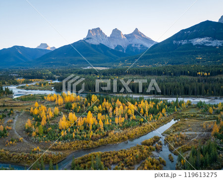 Aerial view of Canadian Rockies mountain range and Bow river forest at dawn in autumn. Canmore, Alberta, Canada. The Three Sisters trio of peaks. 119613275