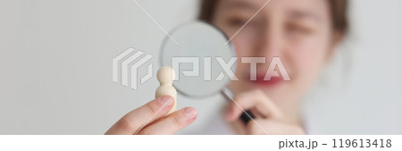 Woman looks at wooden figurine in hand through loupe 119613418