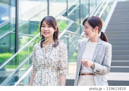 楽しく話しながらオフィスの中を歩く女性ビジネスパーソン 119613828