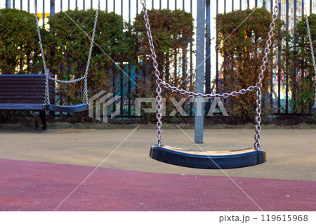 Empty swings on a playground evoke sadness and loneliness, metal chains gently swaying in the wind. Empty playground with swings. Lonely swings on a playground. 119615968
