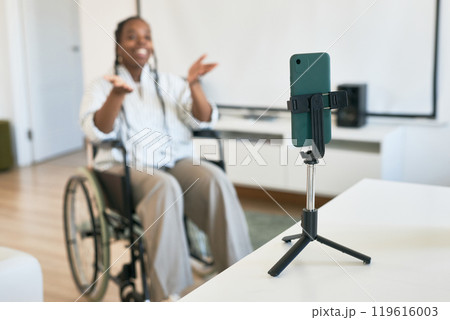 Smiling woman in wheelchair communicating using smartphone on tripod in living room with modern decor, expressing joy and engagement Smiling woman in wheelchair communicating using smartphone on tripod in living room with modern decor, expressing joy and engagement 119616003