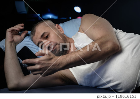 Man with smartphone in bed at night. Handsome man using mobile phone in bed.. Man with smartphone in bed at night. Handsome man using mobile phone in bed.. 119616153